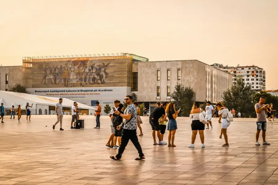 Një shesh publik në Tiranë në perëndim, me njerëz që e kalojnë