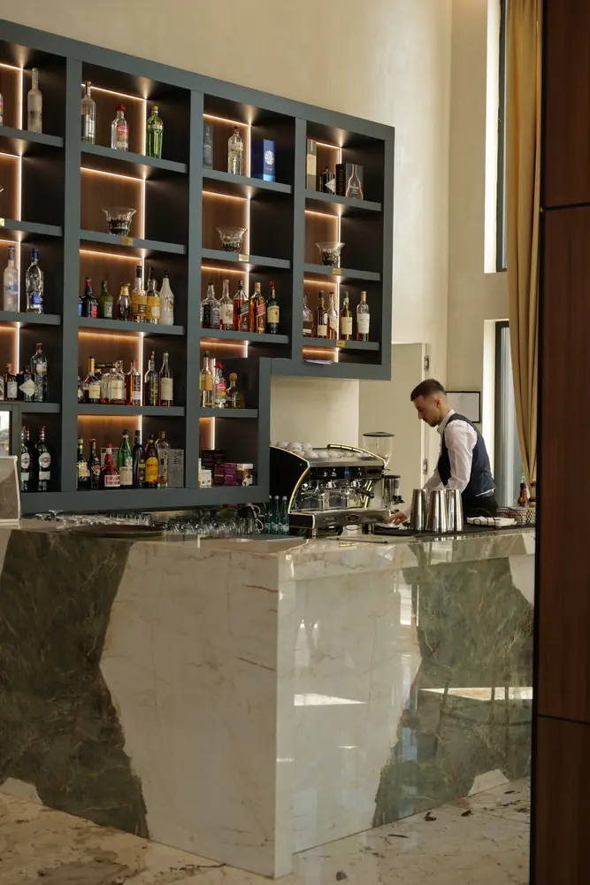 Bari i Mercure Tirana, me rafte të ndriçuara shishesh dhe një barmen në punë